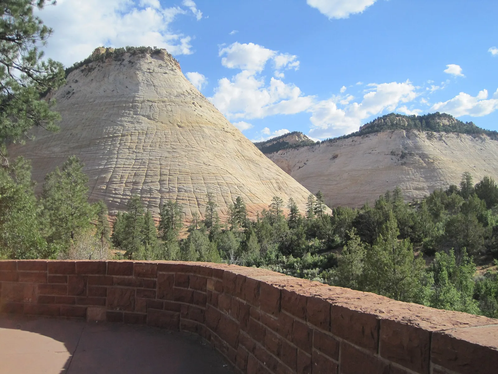 Checkerboard Mesa, a pale cross-hatched sandstone dome, seen from a stone wall along the Zion–Mount Carmel Highway.