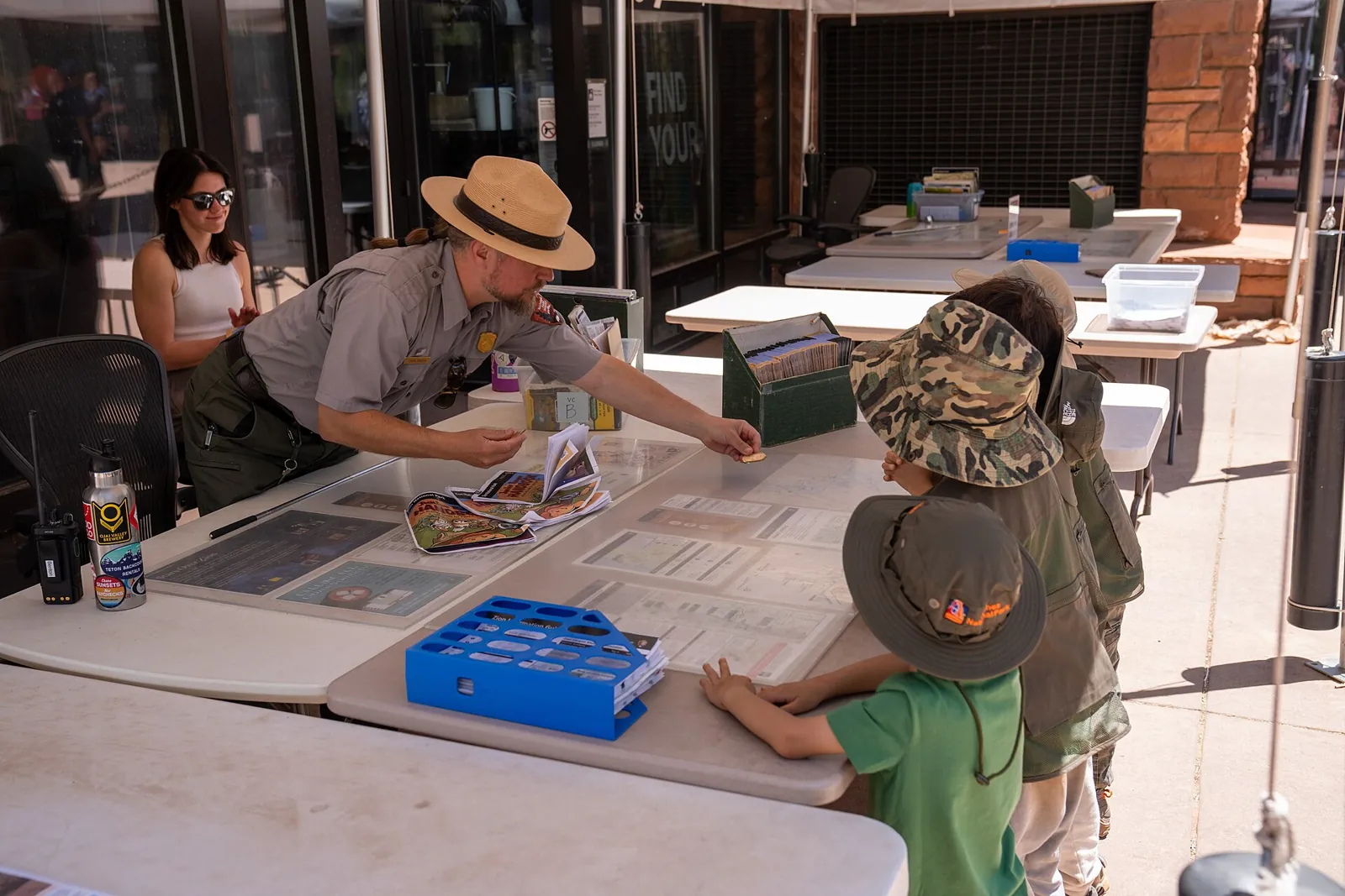 A park ranger at an outdoor desk at Zion Canyon Visitor Center talking with children who are becoming Junior Rangers.