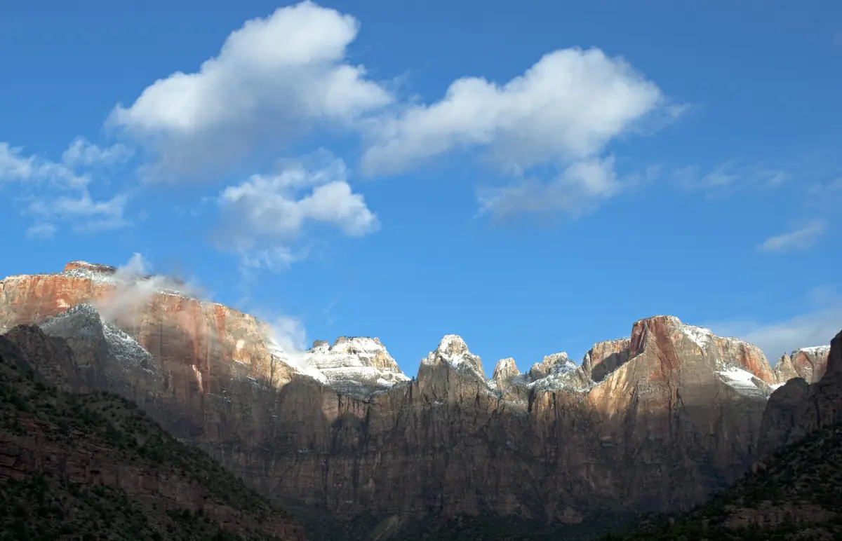 A spring dusting of snow on the peaks above Zion Canyon under white clouds.