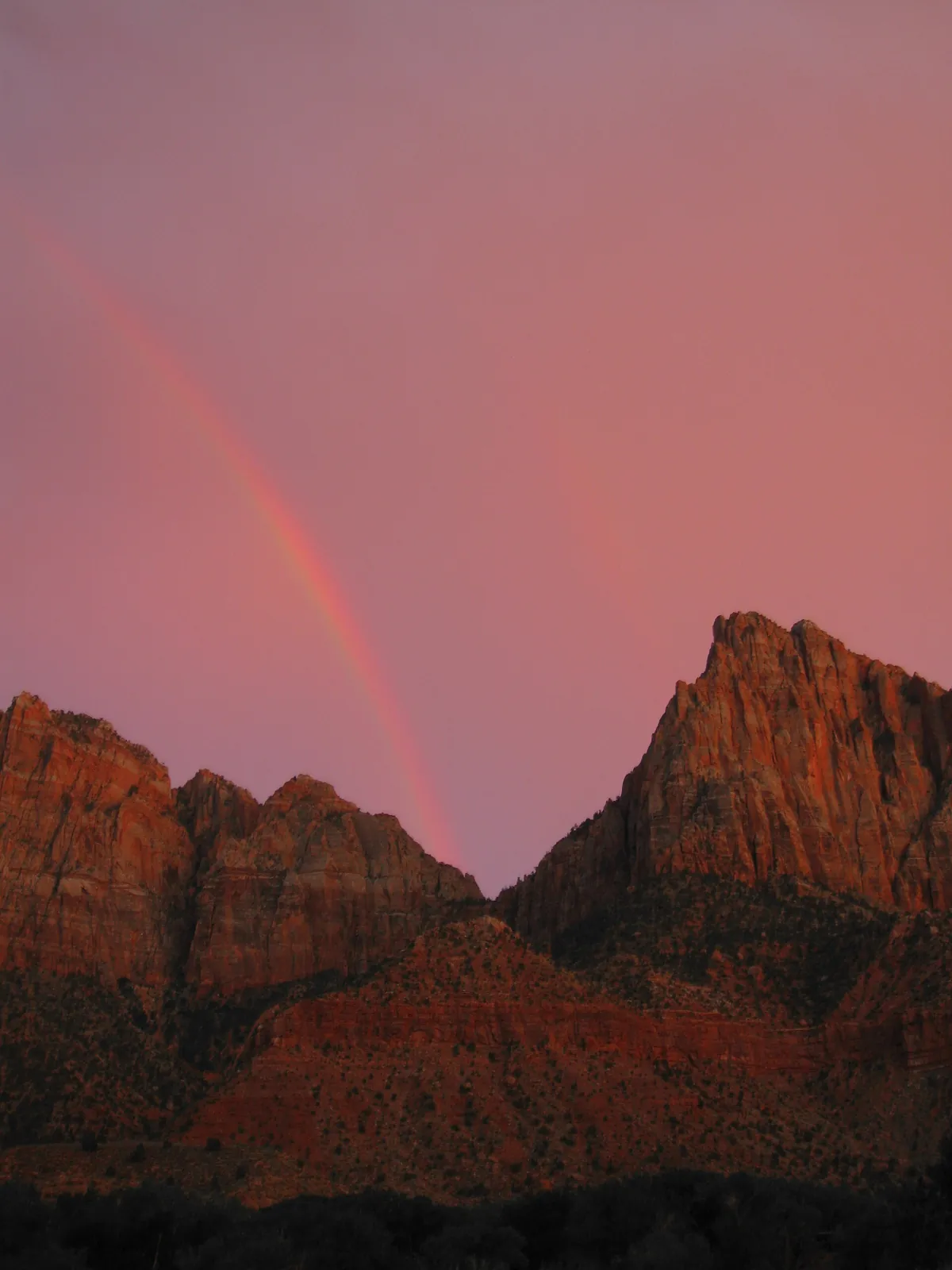 A faint rainbow over red cliffs of The Watchman at sunset after a thunderstorm, Zion National Park.